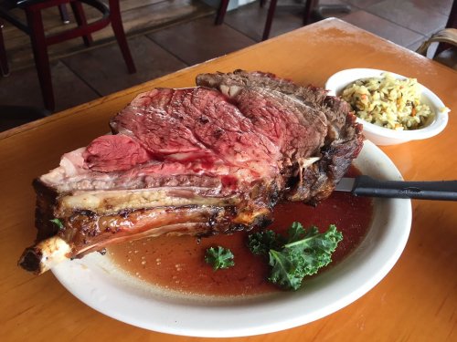 A large, juicy prime rib served on a plate with a side of coleslaw and a garnish of kale.