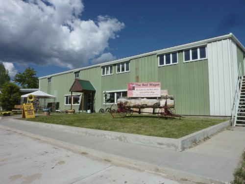 A green and white building with a sign reading "The Red Wagon," featuring a wagon display in front and a blue sky above.