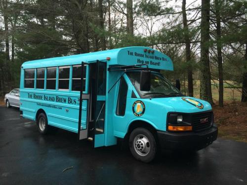 A bright blue bus with "The Rhode Island Brew Bus" written on it, parked in a wooded area.