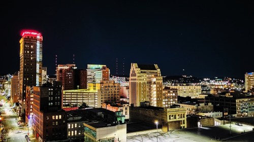 Nighttime cityscape featuring illuminated buildings and a skyline with a mix of modern and historic architecture.