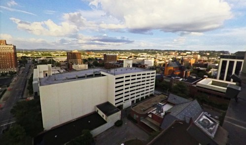 Aerial view of a city skyline with buildings, streets, and a cloudy sky in the background.