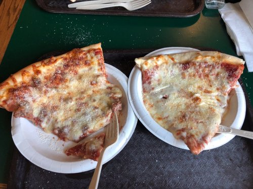 Two large slices of cheese pizza on paper plates, one with a bite taken out, served on a green tray.