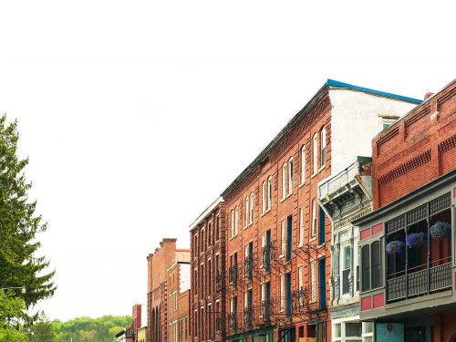 A row of historic brick buildings with a clear sky above, showcasing architectural details and greenery in the background.