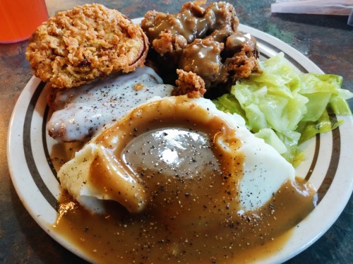 A plate of comfort food featuring fried chicken, mashed potatoes with gravy, lettuce, and a biscuit.