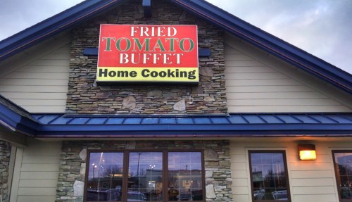 Sign for "Fried Tomato Buffet" featuring "Home Cooking" on a stone building with large windows.