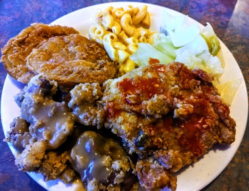 A plate of fried chicken, gravy, fried catfish, macaroni and cheese, and lettuce.