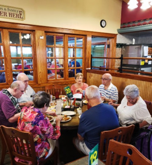 A group of eight people dining at a round table in a cozy restaurant, enjoying their meals and chatting.