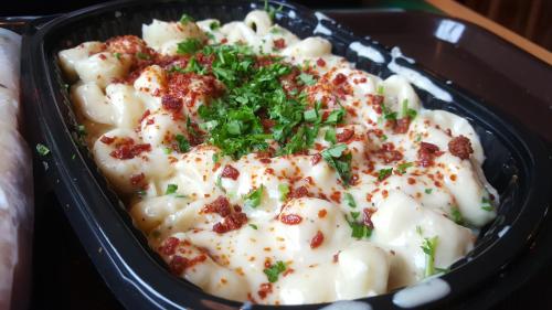 A close-up of creamy pasta topped with herbs and spices in a black takeout container.