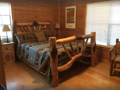 Cozy bedroom with a wooden bed, rustic decor, and natural light from windows.