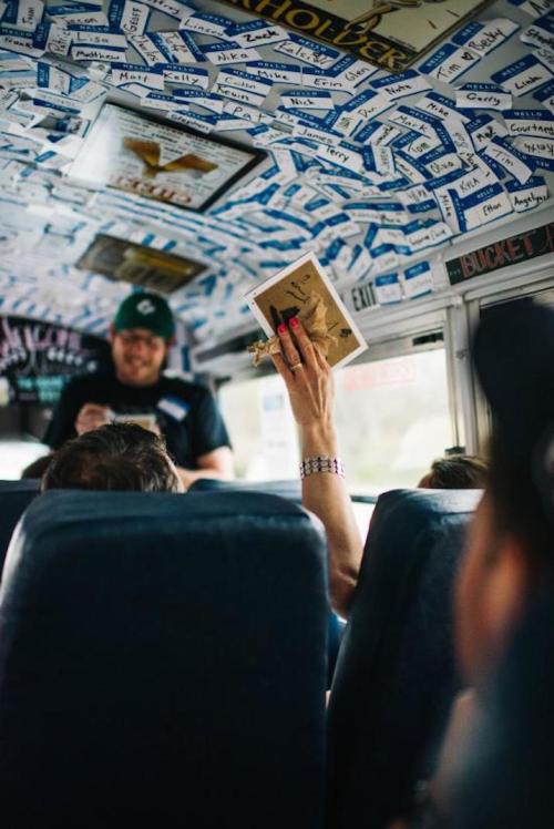 A person holds up a photo in a bus decorated with name tags, while another person stands in the front.