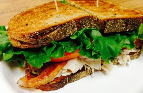 A toasted sandwich with layers of lettuce, tomato, turkey, and bacon, cut in half and held together with toothpicks.