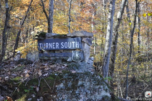 Sign for Turner South trail surrounded by autumn foliage and rocky terrain in a forested area.
