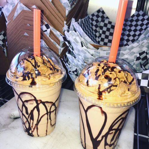 Two frosty drinks topped with whipped cream and chocolate drizzle, served in clear cups with orange straws.