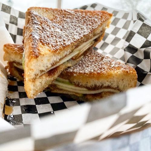 A close-up of a toasted sandwich with powdered sugar, served in a black and white checkered paper basket.