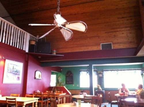 Cozy restaurant interior with wooden ceiling, ceiling fan, and colorful walls; diners seated at wooden tables.