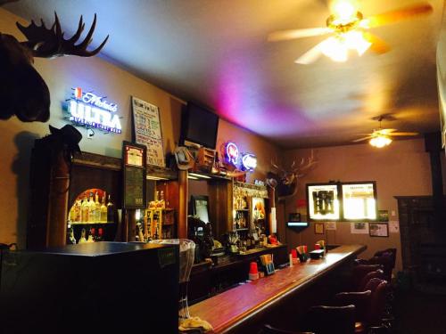 A rustic bar interior featuring wooden decor, a long counter, and mounted antlers, with neon signs and ceiling fans.