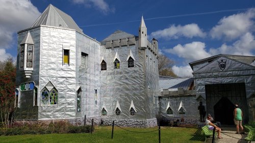 A whimsical castle-like structure covered in shiny silver material, set against a blue sky with fluffy clouds.