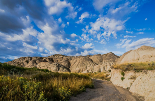 A scenic landscape featuring rolling hills, grassy areas, and a blue sky with fluffy clouds.