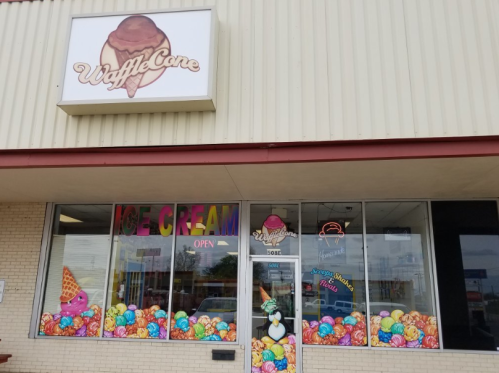 Colorful storefront of "Waffle Cone" ice cream shop, featuring a vibrant display of ice cream graphics and an open sign.