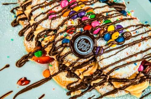 A close-up of colorful, decorated pancakes drizzled with chocolate and topped with sprinkles and a cookie.