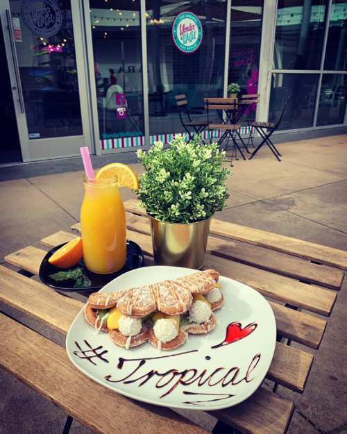 A plate of tropical pastries with a drink and a small plant on a wooden table outside a café.