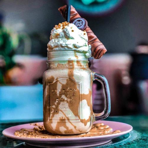 A tall glass jar filled with a creamy milkshake topped with whipped cream, chocolate drizzle, and a wafer stick.