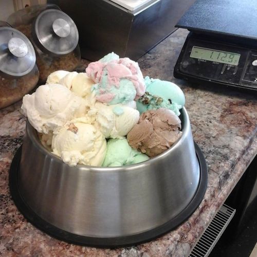 A large metal bowl filled with various colorful ice cream scoops on a countertop next to a digital scale.