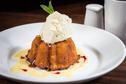 A warm dessert with a golden cake, topped with vanilla ice cream and drizzled with sauce, garnished with a mint leaf.