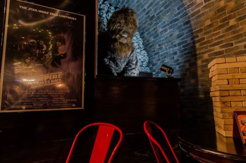A Chewbacca figure stands on a shelf near a "Star Wars: The Empire Strikes Back" poster in a cozy, dimly lit space.