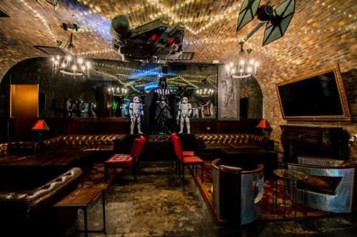 A themed lounge with Star Wars decor, featuring stormtroopers, a large spaceship model, and cozy seating.