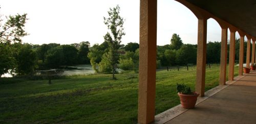 View from a porch with orange columns overlooking a lush green landscape and a calm river.