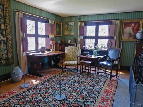 A cozy room with patterned wallpaper, a floral chair, wooden furniture, and art on the walls, featuring a colorful rug.