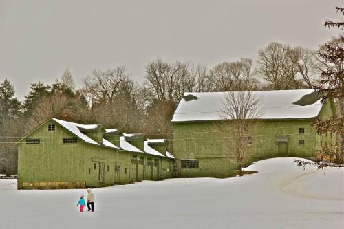 A snowy landscape featuring green barns, with a person and child walking together in the foreground.