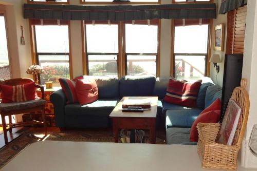 Cozy living room with large windows, a blue couch, red pillows, a wooden table, and a view of the outdoors.
