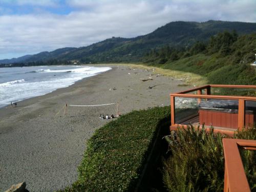 A scenic beach view with gentle waves, a volleyball net, and lush greenery against a backdrop of rolling hills.