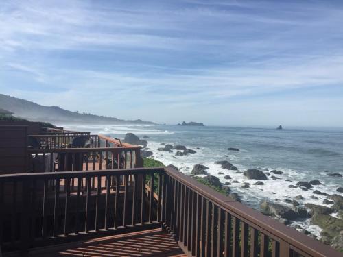 Scenic coastal view with rocky shoreline, gentle waves, and misty hills under a clear blue sky.