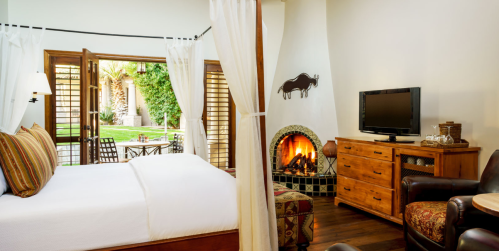 Cozy hotel room with a fireplace, wooden furniture, and large windows opening to a garden view.