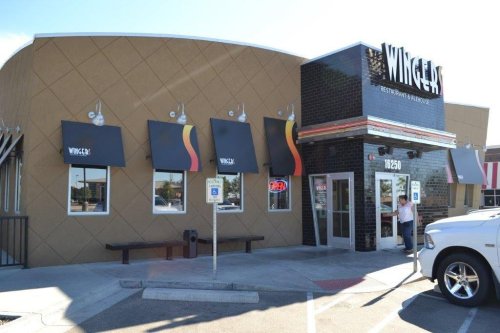 Exterior of Wingsters restaurant featuring a modern design, large windows, and an "Open" sign. Parking area visible.