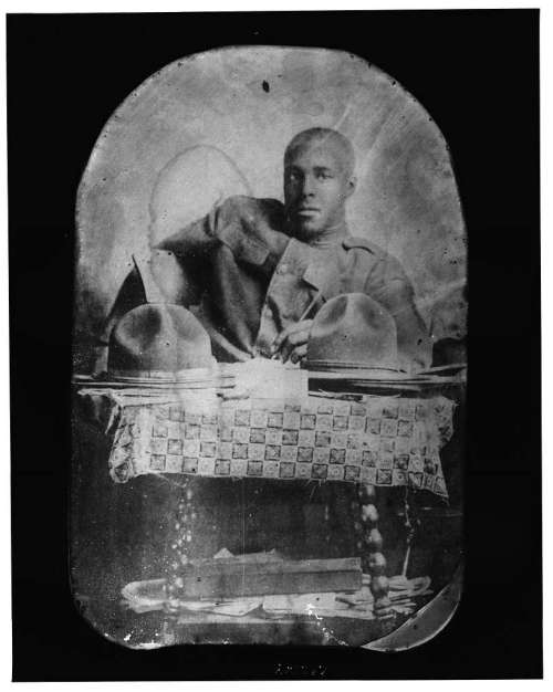 A historical portrait of a seated man in military attire, resting his arm on a table with two helmets.