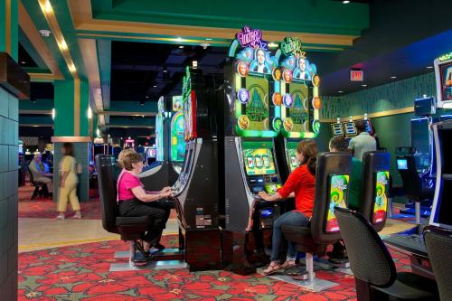 Two women play slot machines in a vibrant casino, surrounded by colorful lights and other gaming machines.