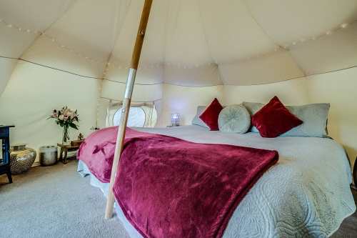Cozy tent interior with a large bed, plush pillows, and soft lighting, creating a warm and inviting atmosphere.
