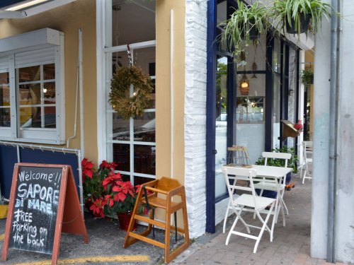 A cozy restaurant entrance with a welcome sign, holiday decorations, and outdoor seating.