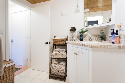 A bright bathroom featuring a towel rack, sink with mirror, and a door leading to another room.