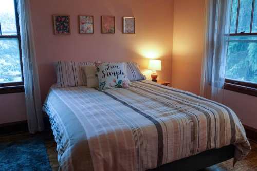 Cozy bedroom with a striped bedspread, decorative pillows, and soft lighting from a bedside lamp.