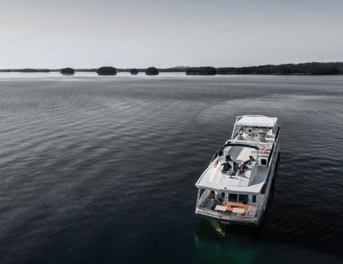 Aerial view of a boat on calm water, with people relaxing on the deck and islands in the background.