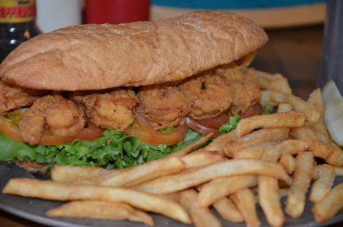 A large sandwich filled with fried shrimp, lettuce, and tomatoes, served with a side of crispy French fries.