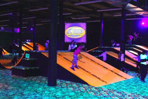Children playing on colorful slides in a dimly lit indoor skate park with neon lights.
