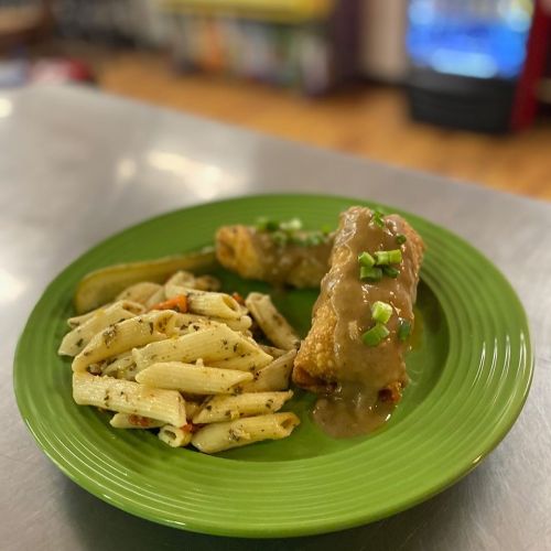 A green plate with pasta salad and a fried roll topped with gravy and green onions.