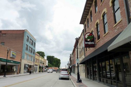 A quiet downtown street lined with brick buildings, shops, and a sign for a restaurant under a cloudy sky.