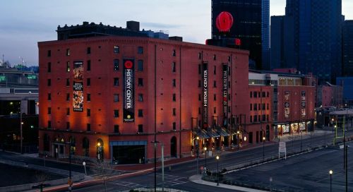 Historic red brick building with large signage, illuminated at dusk, surrounded by cityscape and empty streets.